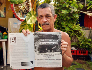 Artist Carlos Alberto Uribe holds a copy of the magazine Contravia, which published an article on the sign he made with bullet casings from the 1999 confrontation between the Revolutionary Armed Forces of Colombia (FARC) and security forces in Capurganá. (Juan Carlos Rocha for Infosurhoy.com)
