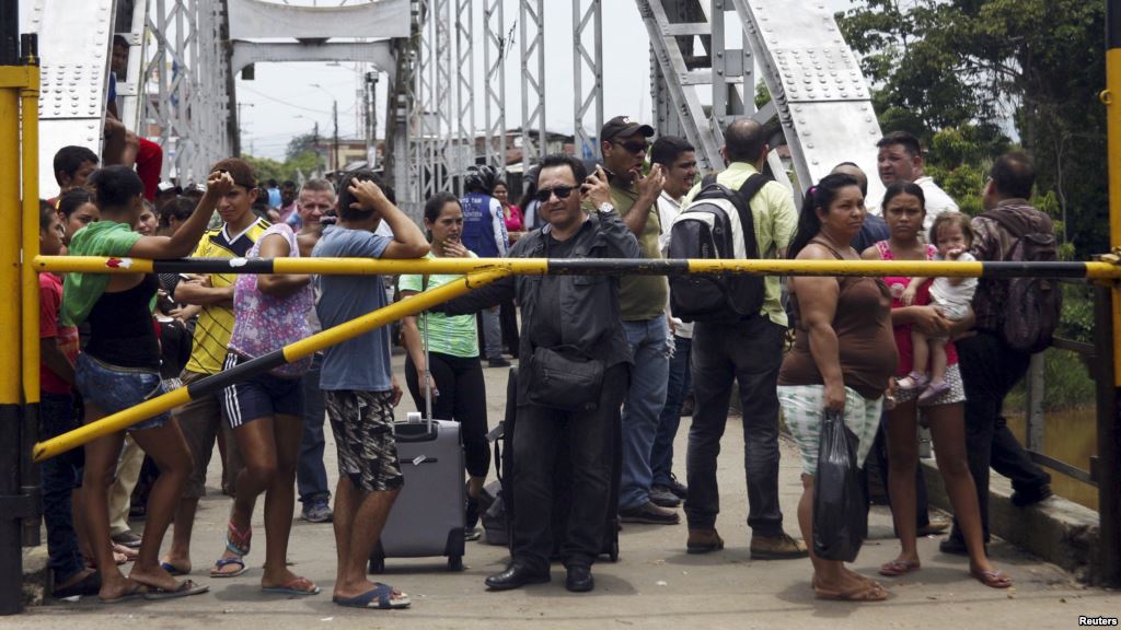 People stand next to a closed gate as they wait to try to cross La Union international bridge, on the border with Colombia at Boca de Grita in Tachira state, Venezuela, Aug. 29, 2015